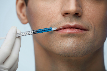 Facial Injection. Closeup Of Beautician Doing Injection In Young Male Patient Lips. Man Face Receiving Beauty Procedure Using Filler Injections. Cosmetology And Beauty Concepts. High Resolutionの写真素材