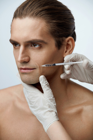 Male Beauty Injection. Portrait Of Handsome Man Receiving Hyaluronic Acid Facial Injections. Closeup Of Cosmetician Injecting Fillers Into Young Man's Face. Plastic Surgery Conceprt. High Resolutionの写真素材