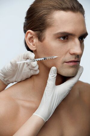 Male Beauty Injection. Portrait Of Handsome Man Receiving Hyaluronic Acid Facial Injections. Closeup Of Cosmetician Injecting Fillers Into Young Man's Face. Plastic Surgery Conceprt. High Resolutionの写真素材