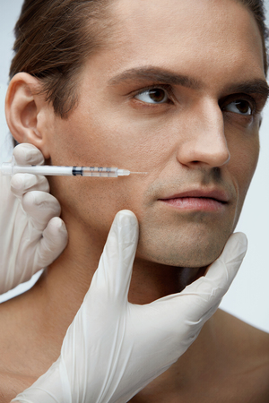 Male Beauty Injection. Portrait Of Handsome Man Receiving Hyaluronic Acid Facial Injections. Closeup Of Cosmetician Injecting Fillers Into Young Man's Face. Plastic Surgery Conceprt. High Resolutionの写真素材