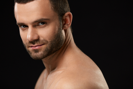 Male Beauty Face. Closeup Of Handsome Sexy Young Man With Stubble Beard And Soft Facial Skin. Portrait Of Beautiful Smiling Man With Beautiful Face On Black Background. High Resolutionの写真素材