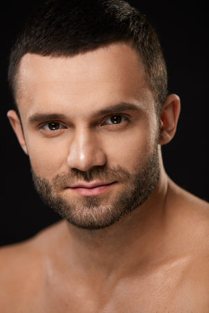 Male Beauty Face. Closeup Of Handsome Sexy Young Man With Stubble Beard And Soft Facial Skin. Portrait Of Beautiful Smiling Man With Beautiful Face On Black Background. High Resolutionの写真素材