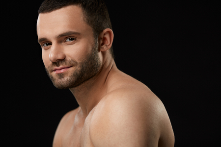 Male Beauty Face. Closeup Of Handsome Sexy Young Man With Stubble Beard And Soft Facial Skin. Portrait Of Beautiful Smiling Man With Beautiful Face On Black Background. High Resolutionの写真素材
