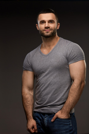 Sexy Young Man Portrait. Closeup Of Handsome Strong Male Model With Muscular Body, Beautiful Face And Beard. Healthy Confident Smiling Guy In Casual Clothes Posing On Grey Background. High Resolutionの写真素材