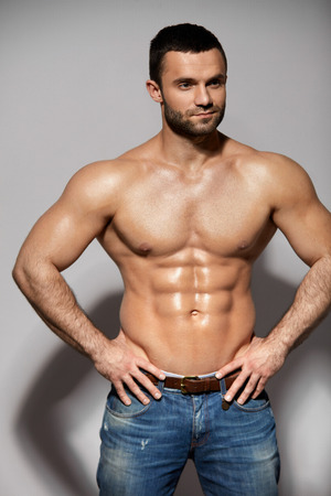 Handsome Smiling Young Man With Sexy Fit Body Posing On Grey Background Indoors. Closeup Portrait Of Healthy Strong Male With Perfect Body Shape And Muscular Abs. Bodybuilding Concept. High Resolutionの写真素材