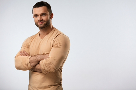 Handsome Man Portrait. Closeup Of Strong Sexy Young Male With Beautiful Face, Fit Muscular Body Standing With HIs Arms Crossed. Attractive Confident Guy On Grey Background. High Resolutionの写真素材