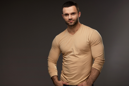 Sexy Young Man Portrait. Closeup Of Handsome Strong Male Model With Muscular Body, Beautiful Face And Beard. Healthy Confident Smiling Guy In Casual Clothes Posing On Grey Background. High Resolutionの写真素材