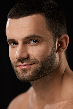 Male Beauty Face. Closeup Of Handsome Sexy Young Man With Stubble Beard And Soft Facial Skin. Portrait Of Beautiful Smiling Man With Beautiful Face On Black Background. High Resolutionの写真素材