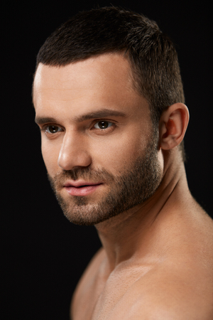 Male Beauty Face. Closeup Of Handsome Sexy Young Man With Stubble Beard And Soft Facial Skin. Portrait Of Beautiful Smiling Man With Beautiful Face On Black Background. High Resolutionの写真素材