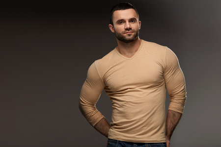 Sexy Young Man Portrait. Closeup Of Handsome Strong Male Model With Muscular Body, Beautiful Face And Beard. Healthy Confident Smiling Guy In Casual Clothes Posing On Grey Background. High Resolutionの写真素材