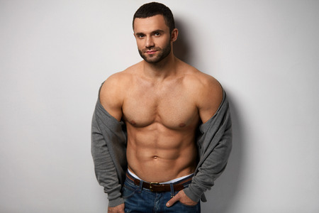 Man Body. Portrait Of Handsome Sexy Young Guy With Fit Muscular Naked Torso And Ideal Abs Muscles Posing With Cardigan Indoors. Closeup Of Hot Fitness Male Model On Grey Background. High Resolutionの写真素材