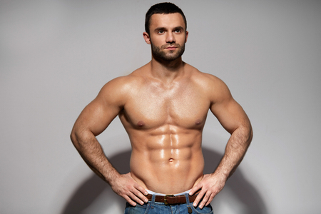 Handsome Smiling Young Man With Sexy Fit Body Posing On Grey Background Indoors. Closeup Portrait Of Healthy Strong Male With Perfect Body Shape And Muscular Abs. Bodybuilding Concept. High Resolutionの写真素材