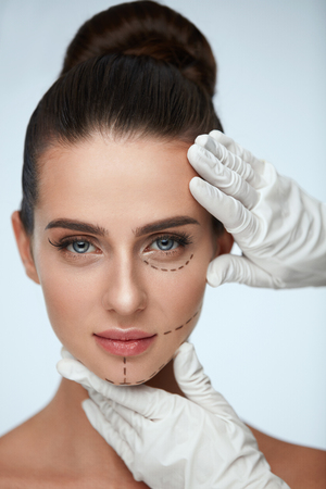 Facial Beauty Treatment. Beautiful Young Female With Smooth Skin, Perfect Makeup And Surgical Lines. Closeup Of Beautician Hands Touching Woman Face Before Plastic Surgery Operation. High Resolutionの写真素材