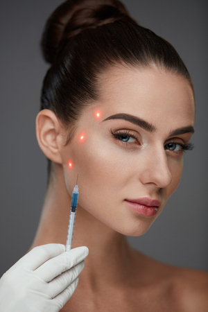 Skin Care. Closeup Of Hands Holding Syringe Near Sexy Young Female Patient's Face. Portrait Of Beautiful Woman Receiving Hyaluronic Acid, Facial Skin Lift Injections. Plastic Surgery. High Resolutionの写真素材