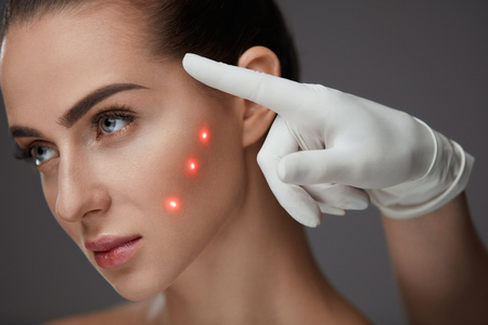 Facial Procedure. Portrait Of Beautiful Female Model With Perfect Skin And Red Points At Face. Closeup Of Beautician Hands Pointing On Young Woman Face. Cosmetic Treatment. High Resolutionの写真素材