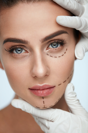 Facial Beauty Treatment. Beautiful Young Female With Smooth Skin, Perfect Makeup And Surgical Lines. Closeup Of Beautician Hands Touching Woman Face Before Plastic Surgery Operation. High Resolutionの写真素材