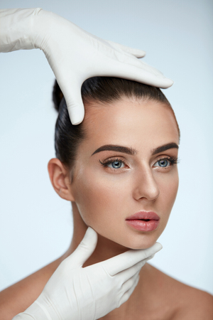 Facial Beauty. Portrait Of Beautiful Young Female With Perfect Makeup And Soft Smooth Skin. Closeup Of Beautician Hands In Gloves Touching Sexy Woman's Face. Plastic Surgery Concept. High Resolutionの写真素材