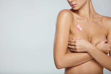 Breast Cancer And Healthcare. Young Woman With Slim Hot Body Holding Her Breasts With Hands On Grey Background. Closeup Sexy Naked Female With Breast Cancer Awareness Ribbon On Chest. High Resolutionの写真素材