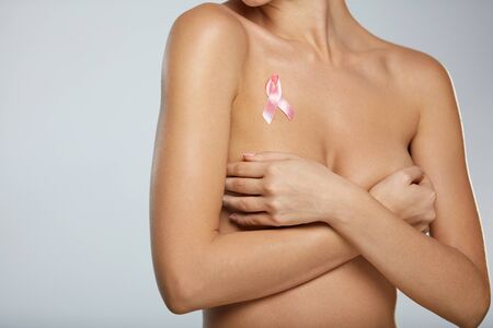 Breast Cancer And Healthcare. Young Woman With Slim Hot Body Holding Her Breasts With Hands On Grey Background. Closeup Sexy Naked Female With Breast Cancer Awareness Ribbon On Chest. High Resolutionの写真素材