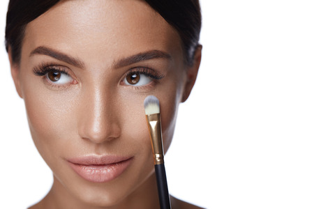 Facial Beauty Makeup. Portrait Of Attractive Young Woman With Soft Skin And Fresh Facial Makeup. Closeup Of Beautiful Sexy Female Using Cosmetic Brush Applying Make-up Cosmetics. High Resolutionの写真素材
