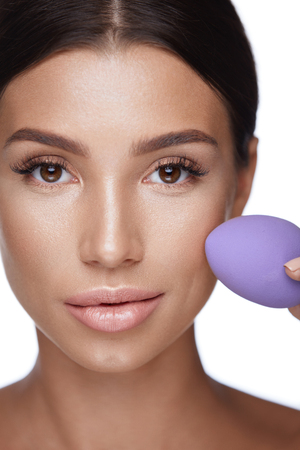 Beauty Face Makeup. Closeup Of Beautiful Young Woman With Professional Facial Makeup And Healthy Skin Applying Foundation Using Cosmetic Sponge Blender. Sexy Female Applying Make-up. High Resolutionの写真素材