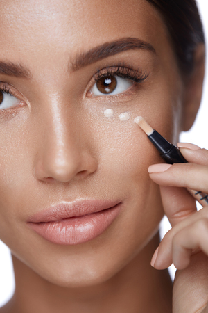 Cosmetics. Portrait Of Sexy Young Woman Applying Concealer On Smooth Soft Facial Skin Under Eyes. Closeup Beautiful Healthy Female Doing Makeup Using Corrector. Beauty Product Concept. High Resolutionの写真素材