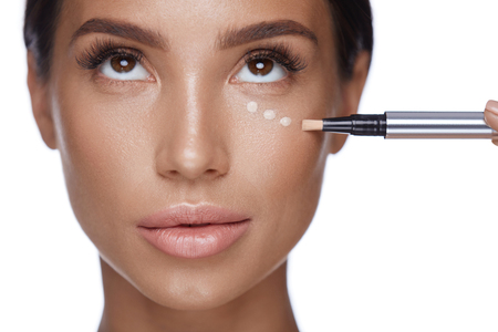 Beauty Woman Face Makeup. Closeup Of Beautiful Young Female Applying Corrector On Skin Under Eyes. Portrait Of Attractive Sexy Girl With Soft Skin Applying Concealer. Cosmetics. High Resolutionの写真素材
