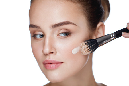 Woman Beauty Face Makeup. Portrait Of Beautiful Young Female Applying Foundation On Face With Cosmetic Brush. Closeup Of Attractive Girl With Smooth Skin And Natural Makeup. Cosmetics. High Resolutionの写真素材