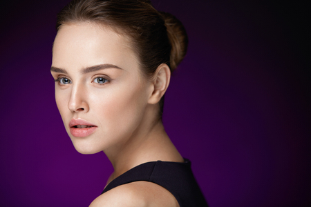 Woman Beauty Cosmetics. Closeup Of Beautiful Sexy Girl With Perfect Face On Dark Purple Background. Portrait Of Young Female With Pure Smooth Skin And Fresh Professional Facial Makeup. High Resolutionの写真素材