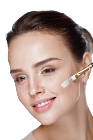 Beauty Cosmetics. Portrait Of Beautiful Young Woman Applying Foundation On Face With Cosmetic Brush. Closeup Of Attractive Female With Smooth Skin And Natural Makeup. Facial Care. High Resolutionの写真素材