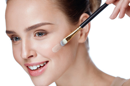 Woman With Beauty Face Applying Makeup. Portrait Of Beautiful Smiling Girl Putting Cream Foundation With Cosmetic Brush On Facial Skin. Closeup Sexy Young Female With Soft Smooth Skin. High Resolutionの写真素材
