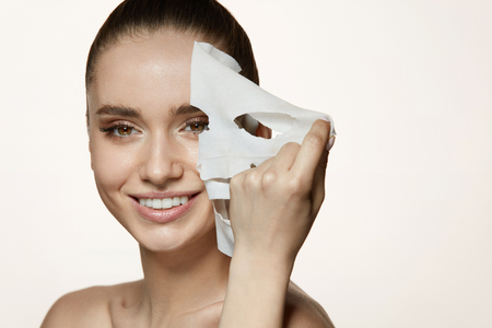 Woman Beauty Face. Closeup Of Smiling Young Female With Fresh Natural Makeup Removing Textile Sheet Mask From Facial Skin. Portrait Of Attractive Happy Girl With White Cosmetic Mask. High Resolution