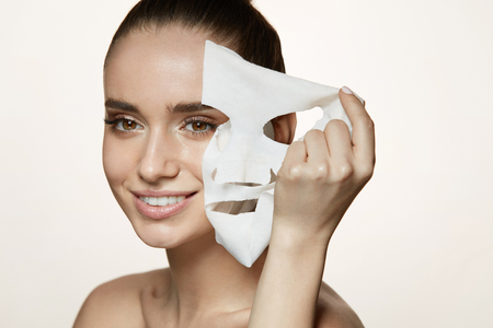 Woman Beauty Face. Closeup Of Smiling Young Female With Fresh Natural Makeup Removing Textile Sheet Mask From Facial Skin. Portrait Of Attractive Happy Girl With White Cosmetic Mask. High Resolution