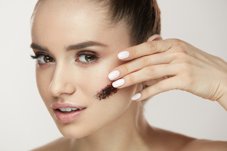 Beauty Treatment. Portrait Of Young Woman Applying Coffee Scrub On Facial Skin. Closeup Of Beautiful Sexy Girl With With Fresh Makeup And Stripe Of Cosmetic Mask On Face. Cosmetology. High Resolutionの写真素材