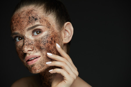 Face Care. Closeup Of Beautiful Woman With Natural Makeup And Skin Exfoliating Coffee Scrub On Beauty Face. Attractive Young Female Applying Mask, Doing Skin Peeling Spa Procedure. High Resolutionの写真素材