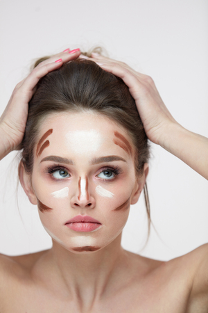 Woman Beauty Face. Closeup Of Beautiful Sexy Girl With Cosmetic Stripes Of Contouring Make-Up Product On Face. Young Female With Soft Skin, Natural Makeup And Hands Near Head. High Resolutionの写真素材