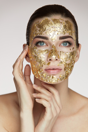 Woman Face Beauty. Portrait Of Beautiful Female Holding Hands Near Head And Golden Mask On Face Skin. Closeup Sexy Girl With Natural Makeup And Skin Cosmetics Product On Facial Skin. High Resolutionの写真素材