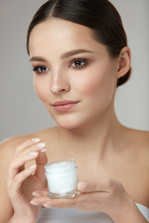 Face Beauty Care. Portrait Of Beautiful Young Woman With Facial Cream Jar In Hand. Closeup Of Sexy Female With Fresh Clean Soft Skin And Natural Makeup With Cosmetic Skin Care Product. High Resolutionの写真素材