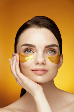 Eye Skin Care Patches. Closeup Of Beautiful Smiling Girl Applying Gold Patches, Collagen Under Eye Mask On Face. Beauty Cosmetics. High Resolutionの写真素材