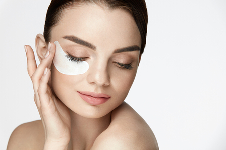 Patch Under Eye. Closeup Of Beautiful Happy Smiling Woman With Moisturizing Under Eye Mask, Face Skin Care Product On White Background. High Resolutionの写真素材