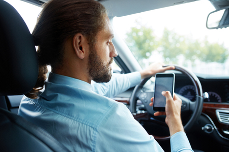 Portrait Of Business Man Driving Car Using Phone. Handsome Elegant Young Businessman In Shirt Holding Smartphone In Hand While Going To Work Luxury Car. High Resolution.の写真素材
