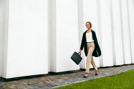 Beautiful Woman Going To Work Walking Near White Wall. Portrait Of Successful Happy Business Woman On Her Way To Work On Street. High Resolution.の写真素材
