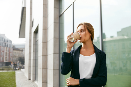 Beautiful Woman Drinking Coffee Outdoors. Portrait Of Business Woman Drinking Hot Drink From Paper Cup Standing Near Office Center On Street. High Quality Image.の写真素材