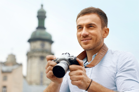 Male Photographer Taking Photos On Camera On Street. Close Up Portrait Of Happy Young Man In Shirt Using Camera, Making Photos During His Travel. High Resolution.の写真素材