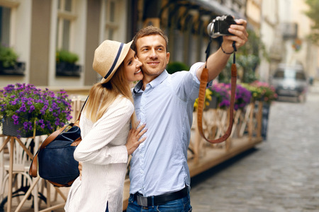 Tourist Couple In Love Taking Photos During Travel. Smiling Young Man And Beautiful Happy Woman In Stylish Clothes Taking Selfies Photo On Camera On Street. High Resolution.の写真素材