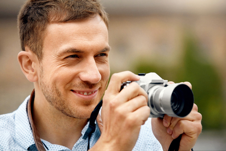 Male Photographer Taking Photos On Camera On Street. Close Up Portrait Of Happy Young Man In Shirt Using Camera, Making Photos During His Travel. High Resolution.の写真素材