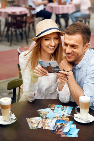 Beautiful Happy Couple In Outdoor Cafe. Smiling Young Man And Happy Woman With Coffee Looking At Postcards Sitting At Table And Enjoying Travel Vacation On Weekend. Tourism. High Quality Image.の写真素材