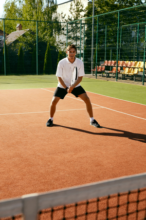 Sports. Male Player Playing Tennis Outdoors. Portrait Of Handsome Attractive Young Man In Stylish White T-shirt Training On Open Court In Summer. Healthy Lifestyle. High Quality Image.の写真素材