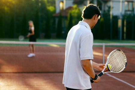 Young People Playing Tennis Outdoors. Healthy Active Man And Woman Holding Rackets In Hands Playing Tennis Match On Open Court On Sunny Summer Day. Sports And Lifestyle. High Resolution.の写真素材