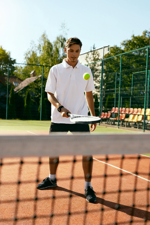 Sports. Male Player Playing Tennis Outdoors. Portrait Of Handsome Attractive Young Man In Stylish White T-shirt Training On Open Court In Summer. Healthy Lifestyle. High Quality Image.の写真素材